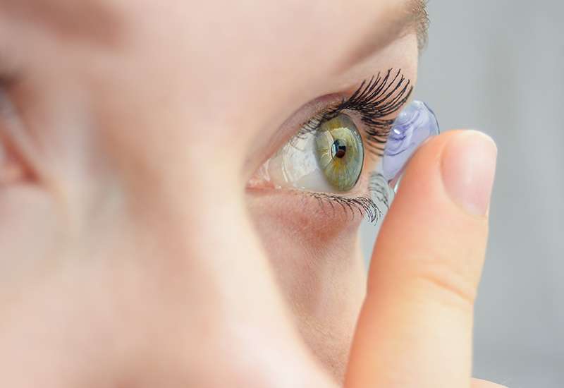 Close-up of a person inserting a contact lens into their eye, focusing on the eye's green iris.