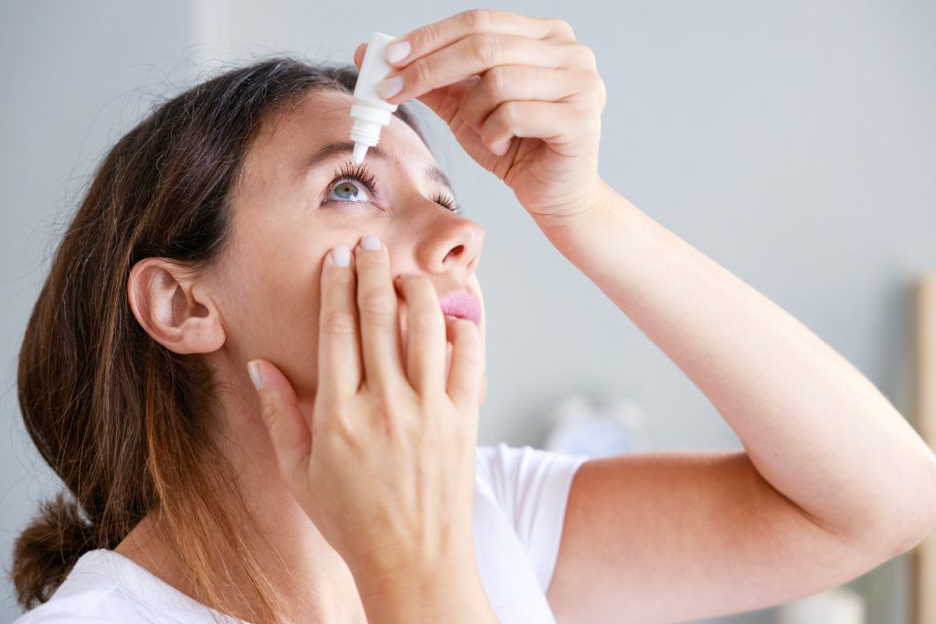 a young woman tilts her head back and inserts an eye drop.