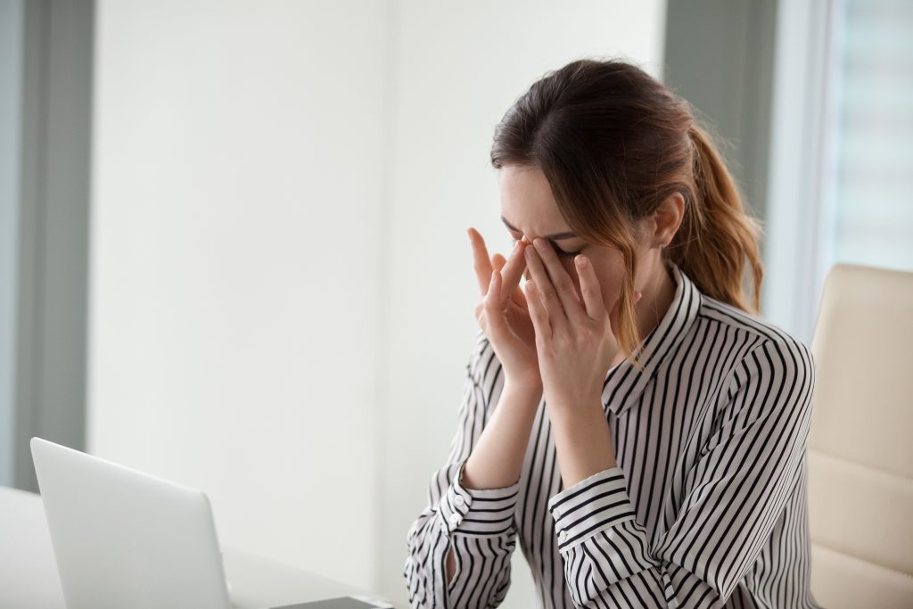 a woman sitting in front of a laptop, touching her eyes in discomfort