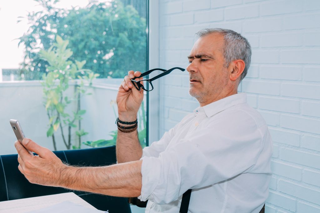 A grey-haired man holds his phone at arm’s length, struggling to read.