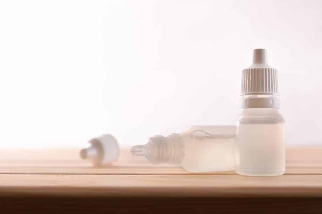 Two bottles of clear eye drops on a wooden tabletop.