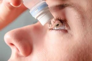 Close-up image of a woman applying eye drops to her left eye.